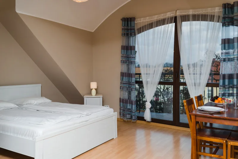 wnętrze apartamentu z widokiem na łóżko oraz okno balkonowe z widokiem na pole