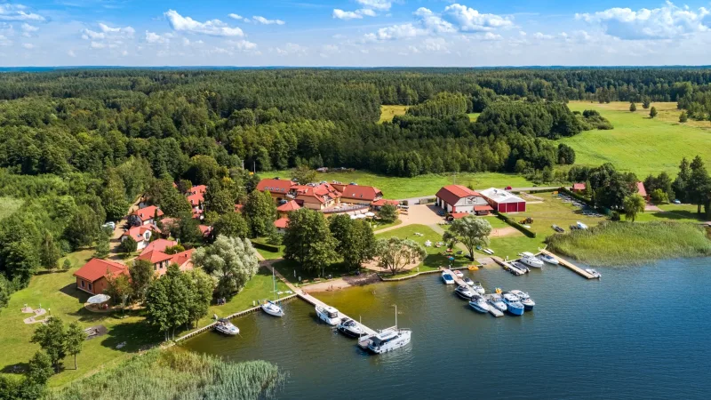Zdjęcie z lotu ptaka - zabudowania hotelowe nad jeziorem, przy pomostach żaglówki